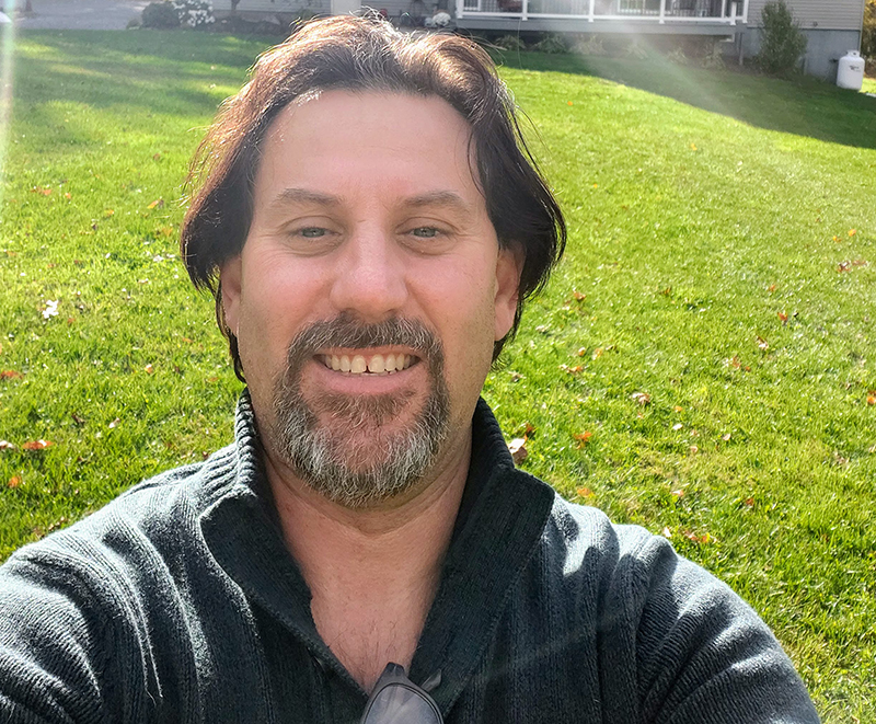 Man wearing a black collared shirt taking a selfie with grass in the background